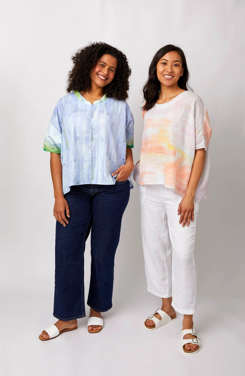 Two women wearing colorful tops and pants standing against a white background