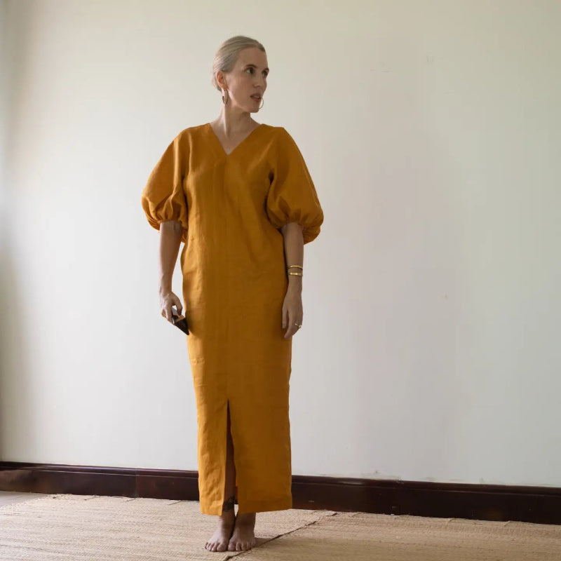 person wearing a mustard yellow dress standing against a plain wall.