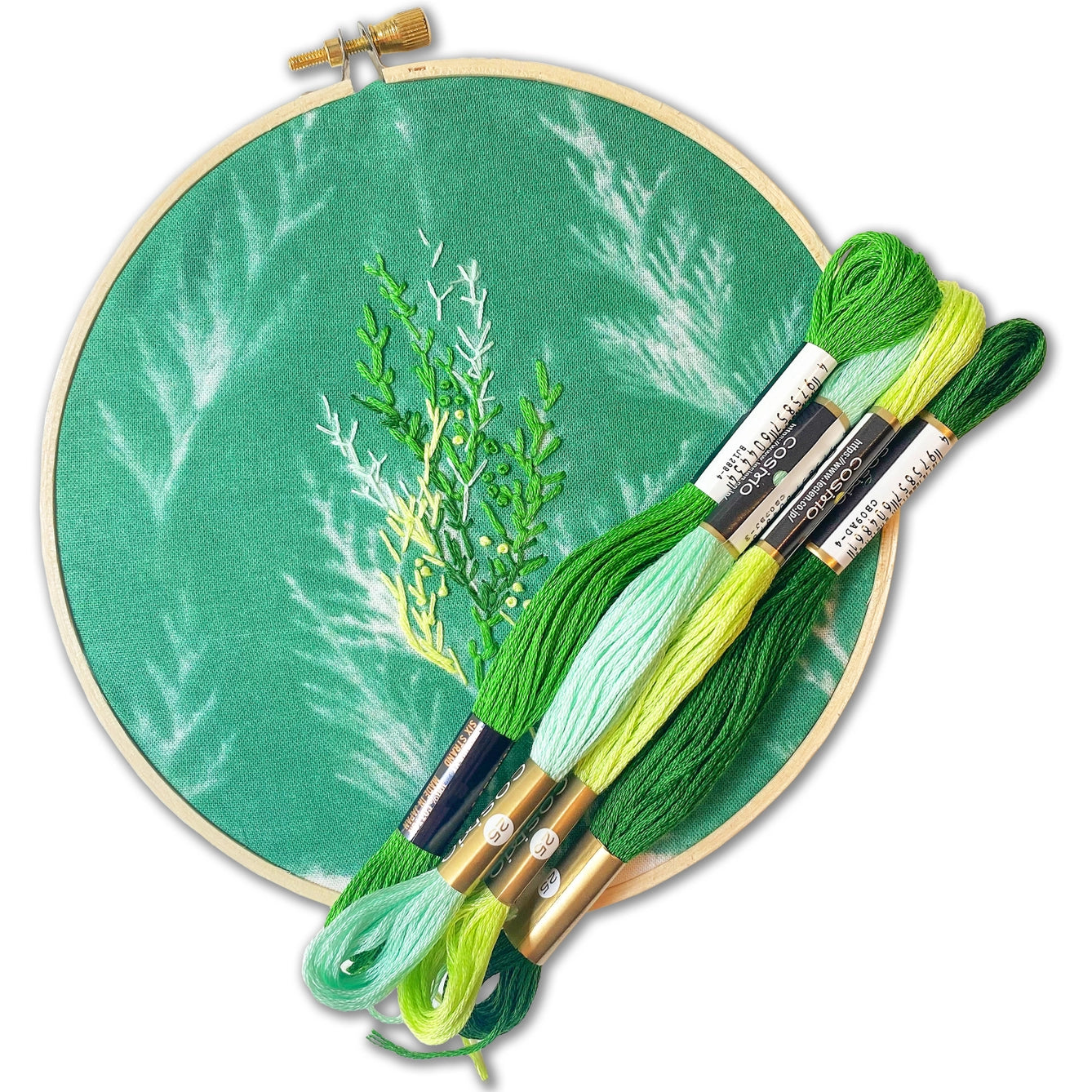 Embroidery hoop with green fabric and embroidered leaves, accompanied by skeins of embroidery thread.