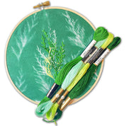 Embroidery hoop with green fabric and embroidered leaves, accompanied by skeins of embroidery thread.