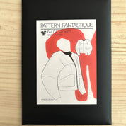 Framed sewing pattern for a jacket with red and white design on a wooden surface
