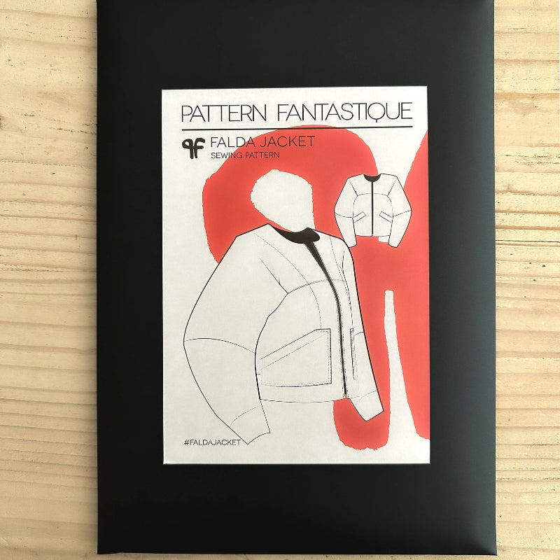 Framed sewing pattern for a jacket with red and white design on a wooden surface