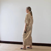 person wearing a gold dress standing against a plain white wall.