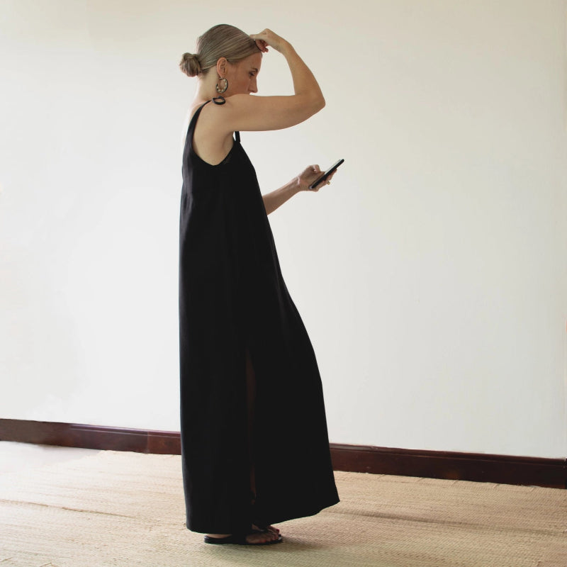 person in a long black dress standing against a plain wall.