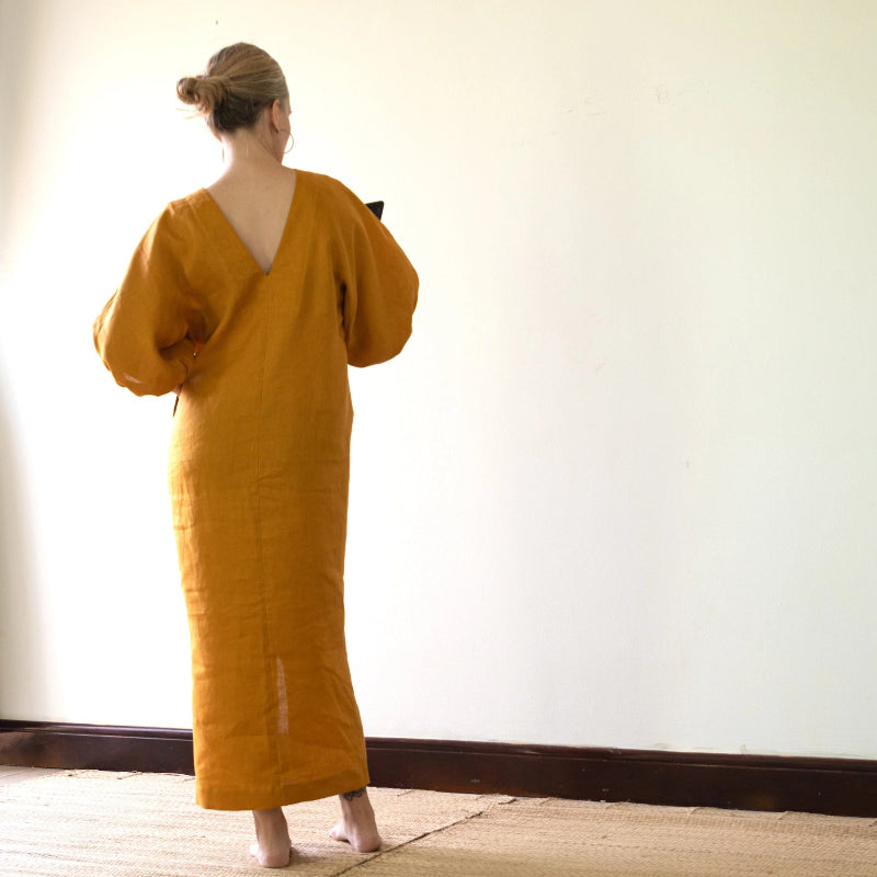 Person wearing a mustard yellow dress standing against a white wall.