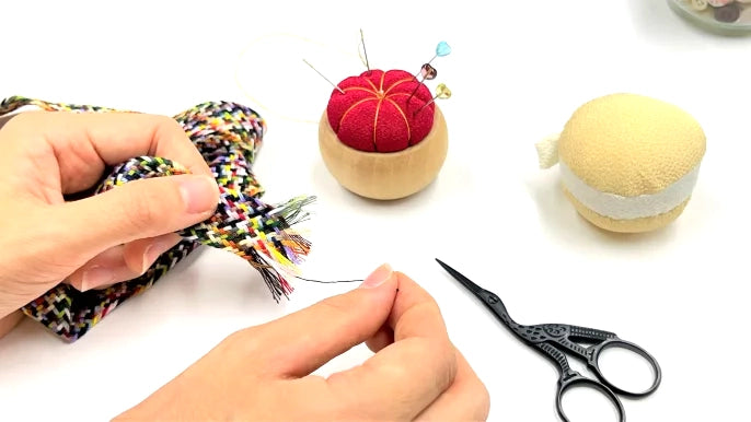 Person threading a needle with sewing tools on a white background