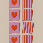 Fabric square labels with red hearts and pink/red stripes on a beige background