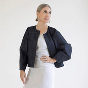 person wearing a dark denim jacket over a white top on a plain background