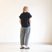 Person wearing a black top and gray pants standing against a white wall.