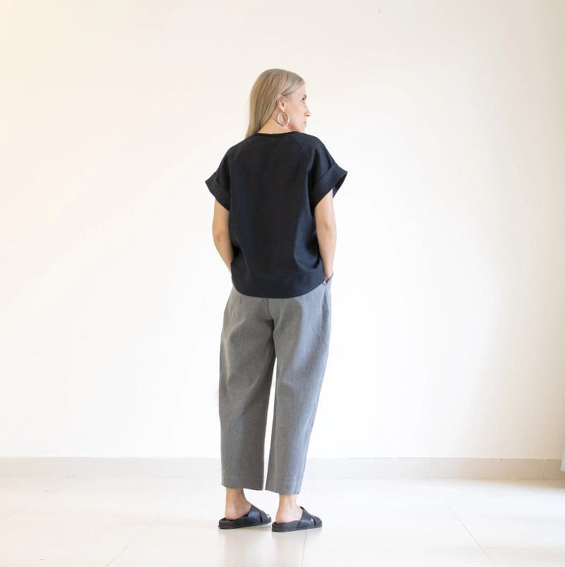 Person wearing a black top and gray pants standing against a white wall.