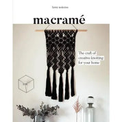 Book cover with black text 'macrame' and a black macrame wall hanging on a white wall with other decor around.