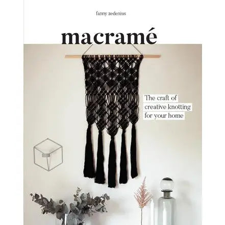 Book cover with black text 'macrame' and a black macrame wall hanging on a white wall with other decor around.