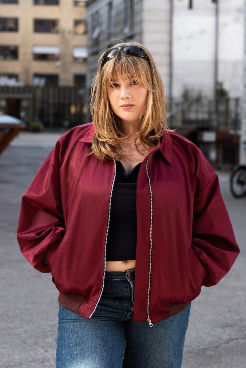 Person wearing a red jacket and blue jeans standing in an urban setting