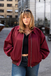 Person wearing a red jacket and blue jeans standing in an urban setting