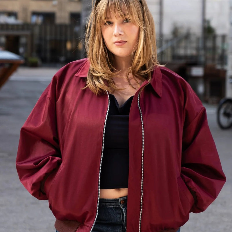 Person wearing a red jacket and blue jeans standing in an urban setting