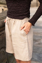 Person wearing a dark textured sweater and light beige shorts with a blurred background