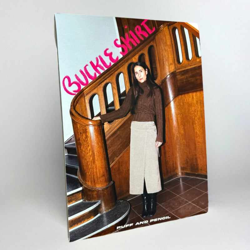 A sewing pattern for a long low-waisted wrap skirt with two buckles at the front side, wide waistband, and asymmetric front overlap, including a snap fastener and eyelets for a belt buckle.