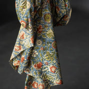 A draped piece of fabric with a dense floral and botanical pattern in muted blue, olive green, rust red, and cream, set against a dark gray background.