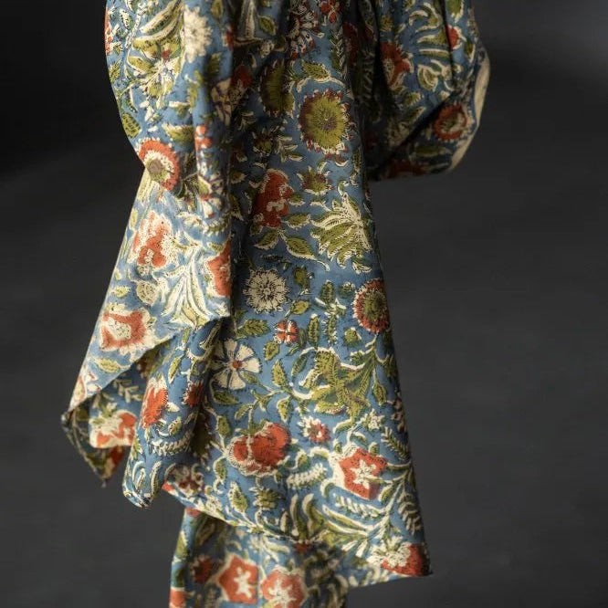A draped piece of fabric with a dense floral and botanical pattern in muted blue, olive green, rust red, and cream, set against a dark gray background.