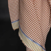 A close-up of a gingham fabric with a brown and white checkered pattern and a contrasting striped border in yellow, blue, and white, draped against a dark background.