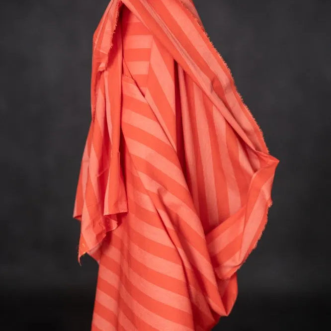 Coral-colored fabric with striped pattern draped over a black background