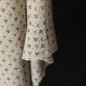 Close-up of a cream-colored cotton fabric with a small brown floral pattern, draped against a solid black background.