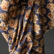 A close-up of draped fabric with an allover floral block-print pattern in navy blue, beige, and rust orange.