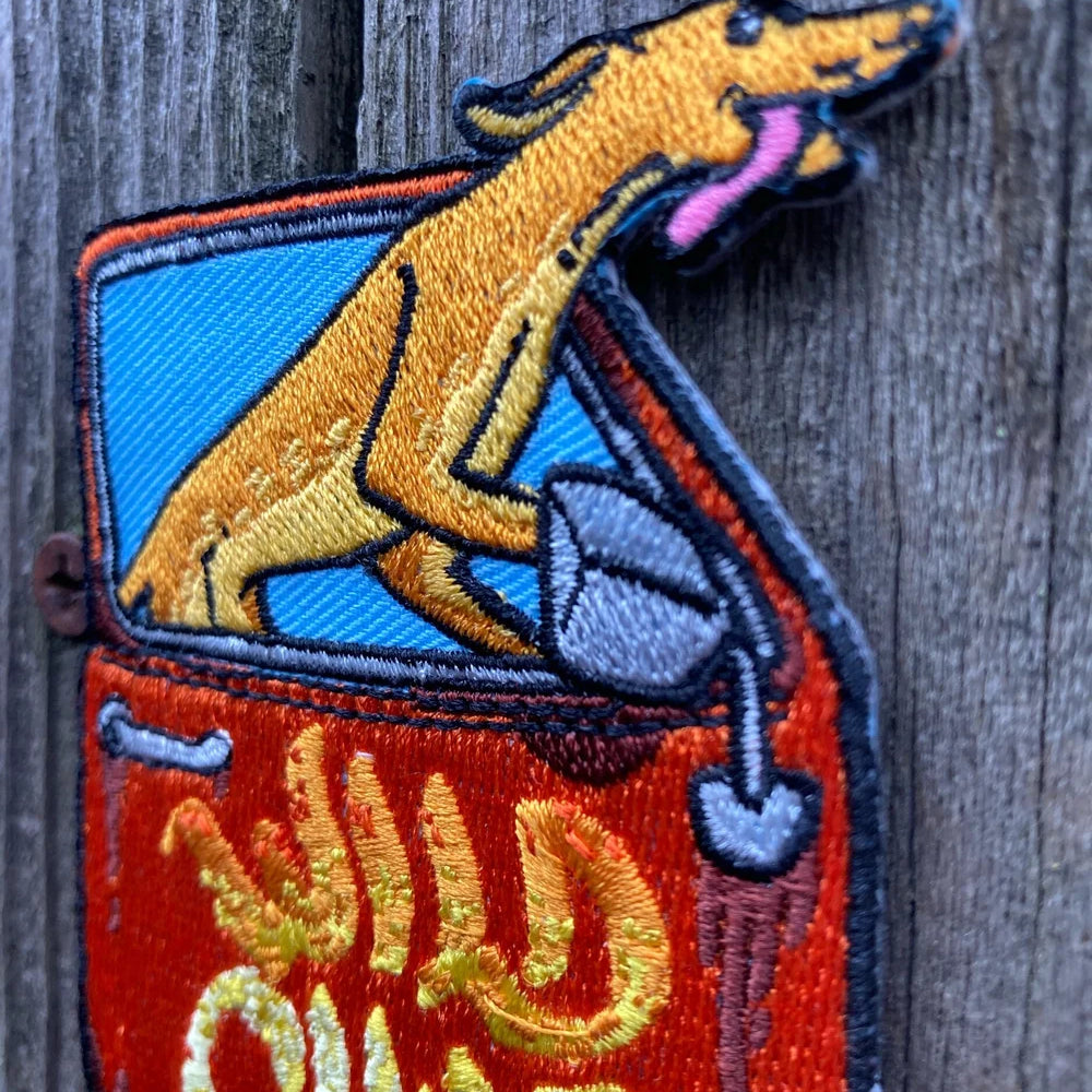 Embroidered patch of a dog in an open suitcase with 'Wild Child' text on a wooden surface