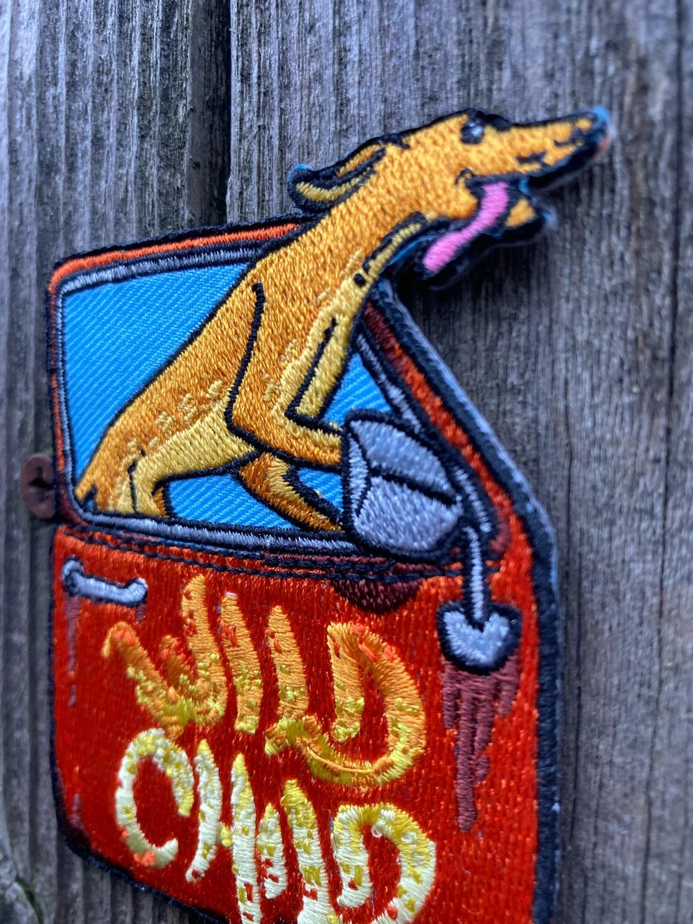 Embroidered patch of a dog in an open suitcase with 'Wild Child' text on a wooden surface