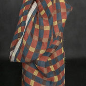 A close-up of a draped fabric or textile with a diagonal plaid/check pattern in muted red, blue, yellow, and brown tones against a dark background.