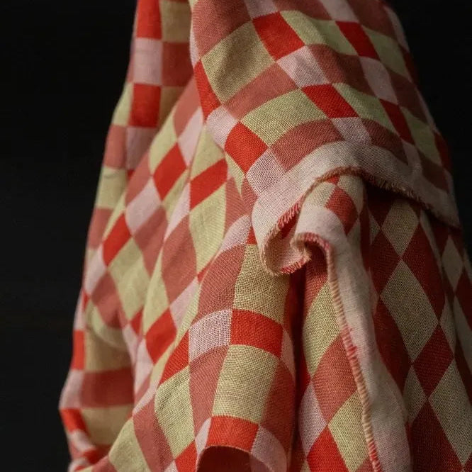 A close-up of draped fabric with a red and pale yellow-orange checkered pattern against a dark background.