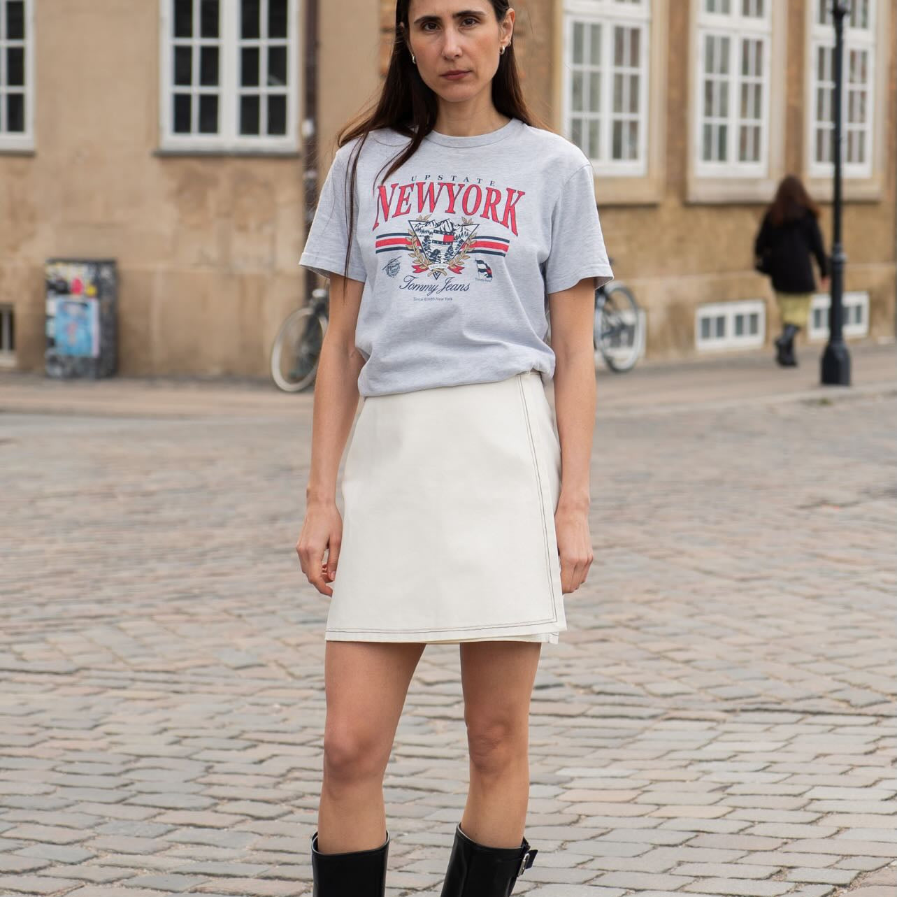 Person wearing a 'New York' t-shirt and white skirt on a cobblestone street.