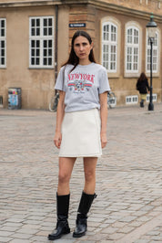 Person wearing a 'New York' t-shirt and white skirt on a cobblestone street.