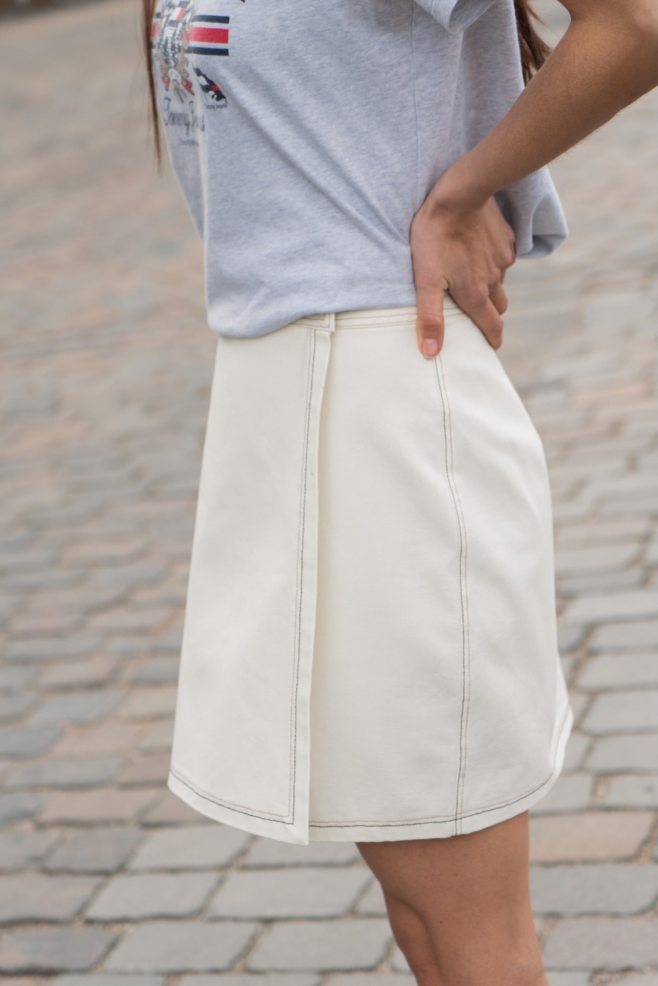 Person wearing a light gray shirt and white skirt on a blurred street background