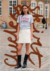 Person wearing a 'New York' t-shirt and white skirt standing in front of artistic wall graffiti.