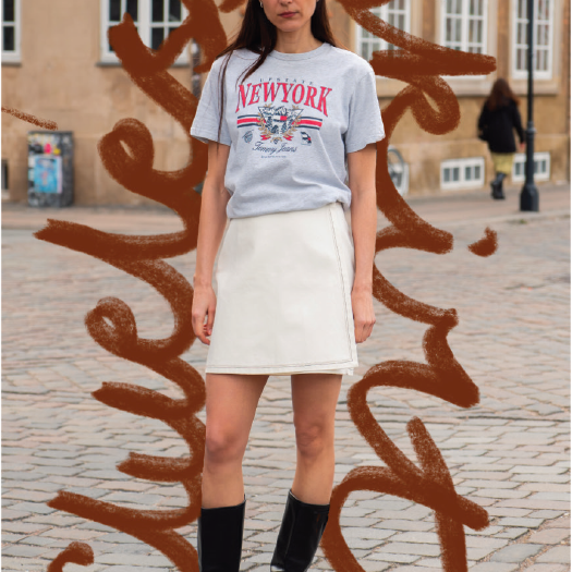 Person wearing a 'New York' t-shirt and white skirt standing in front of artistic wall graffiti.