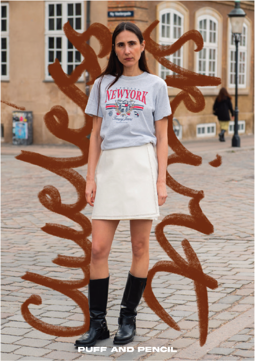 Person wearing a 'New York' t-shirt and white skirt standing in front of artistic wall graffiti.