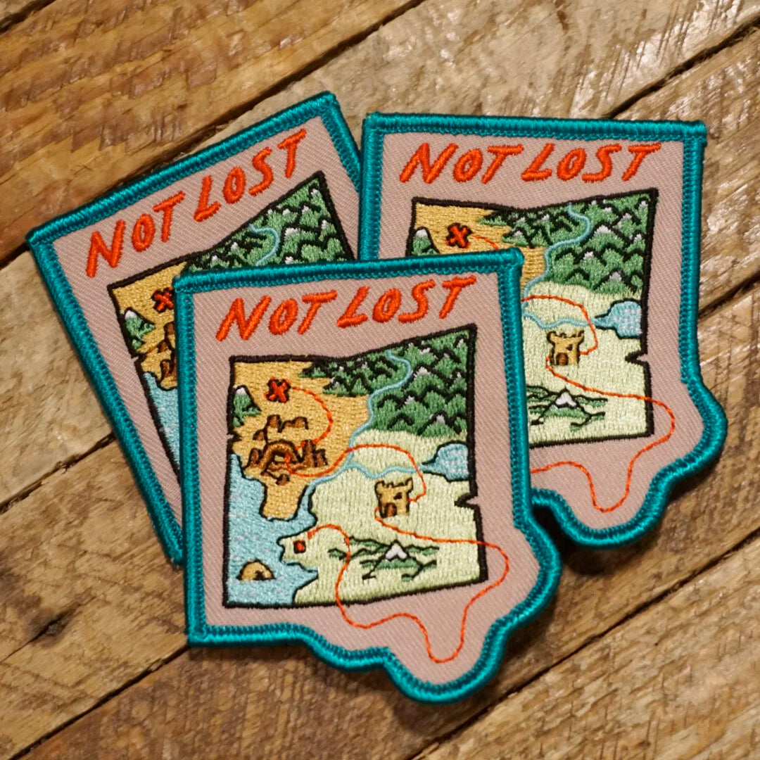 Three 'Not Lost' map patches on a wooden surface