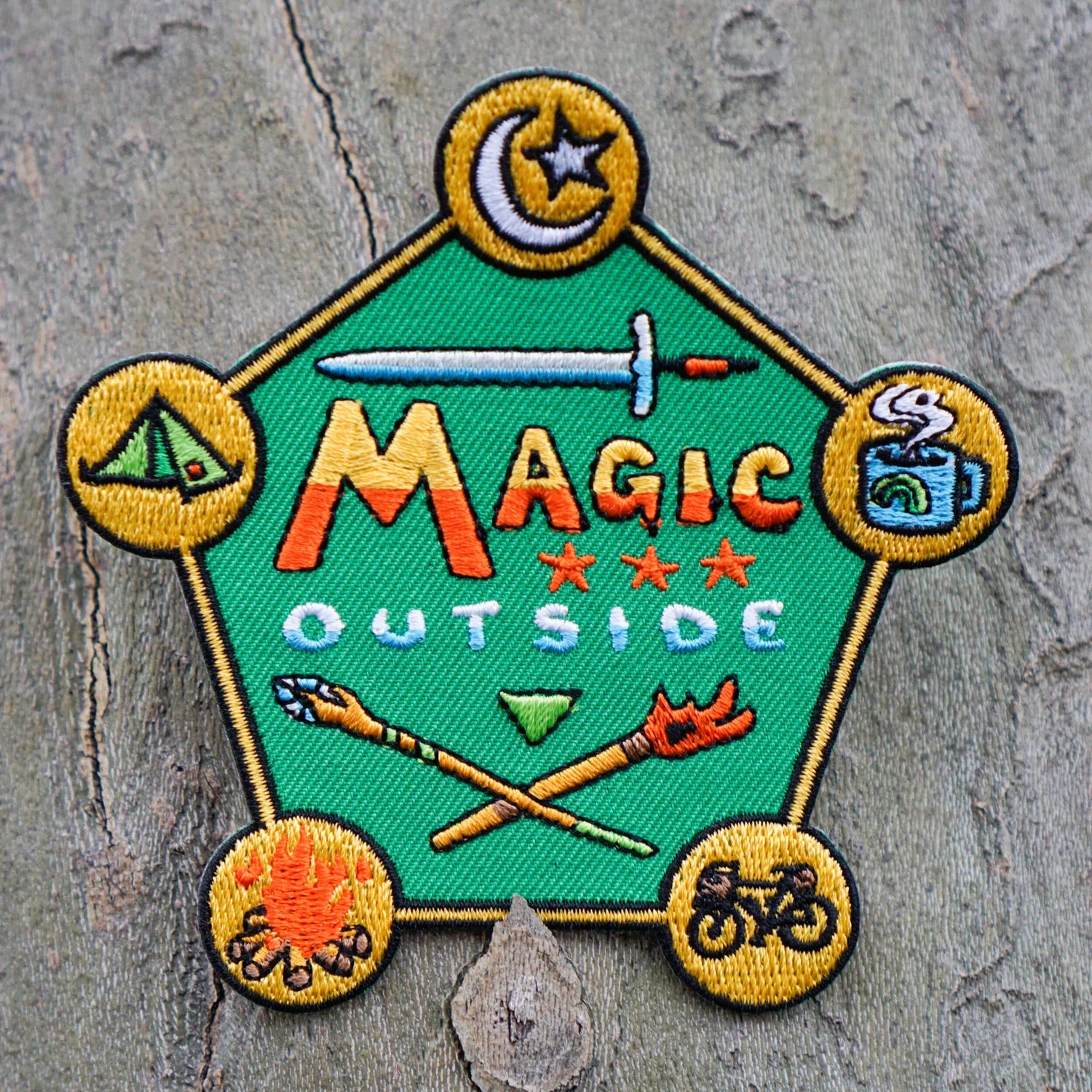 Embroidered patch with 'Magic Outside' text and camping-themed icons on a textured surface.