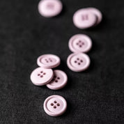 Several small round four-hole buttons in a pale pink or dusty mauve color scattered on a dark textured fabric background.
