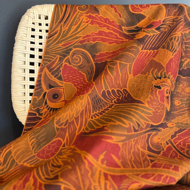 Close-up of a fabric with intricate bird and floral pattern on a wicker chair.