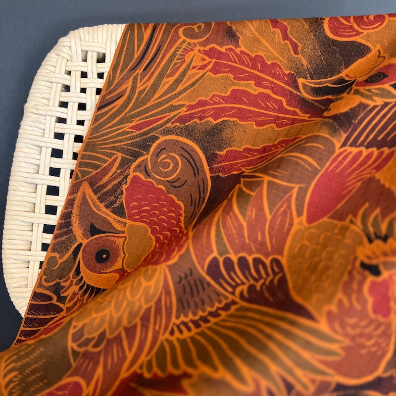 Close-up of a fabric with intricate bird and leaf patterns on a white woven chair.