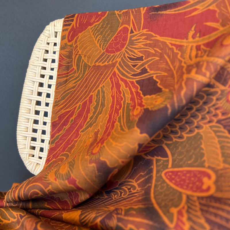Close-up of rust toned patterned fabric with a wicker chair on a dark background