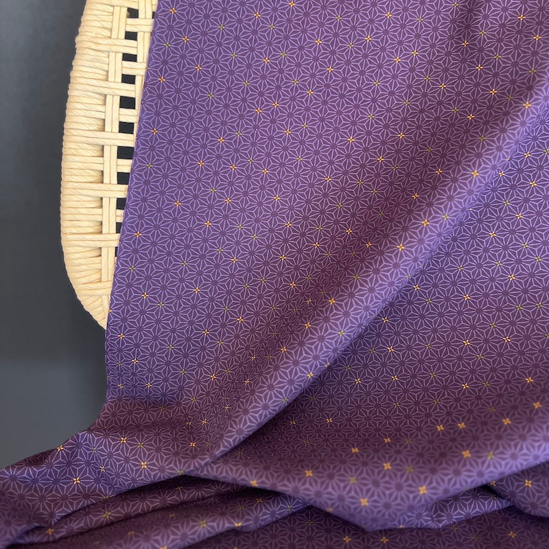 Purple fabric with a geometric pattern draped over a wicker chair on a dark background.