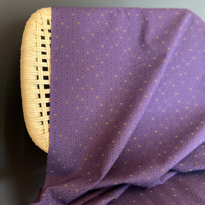 Purple fabric with a geometric pattern draped over a wicker chair on a dark background.