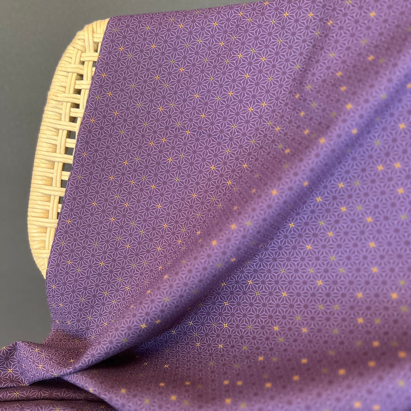 Purple fabric with a geometric pattern draped over a wicker chair on a dark background.