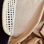 Close-up of a textured beige fabric on a woven wicker chair corner.