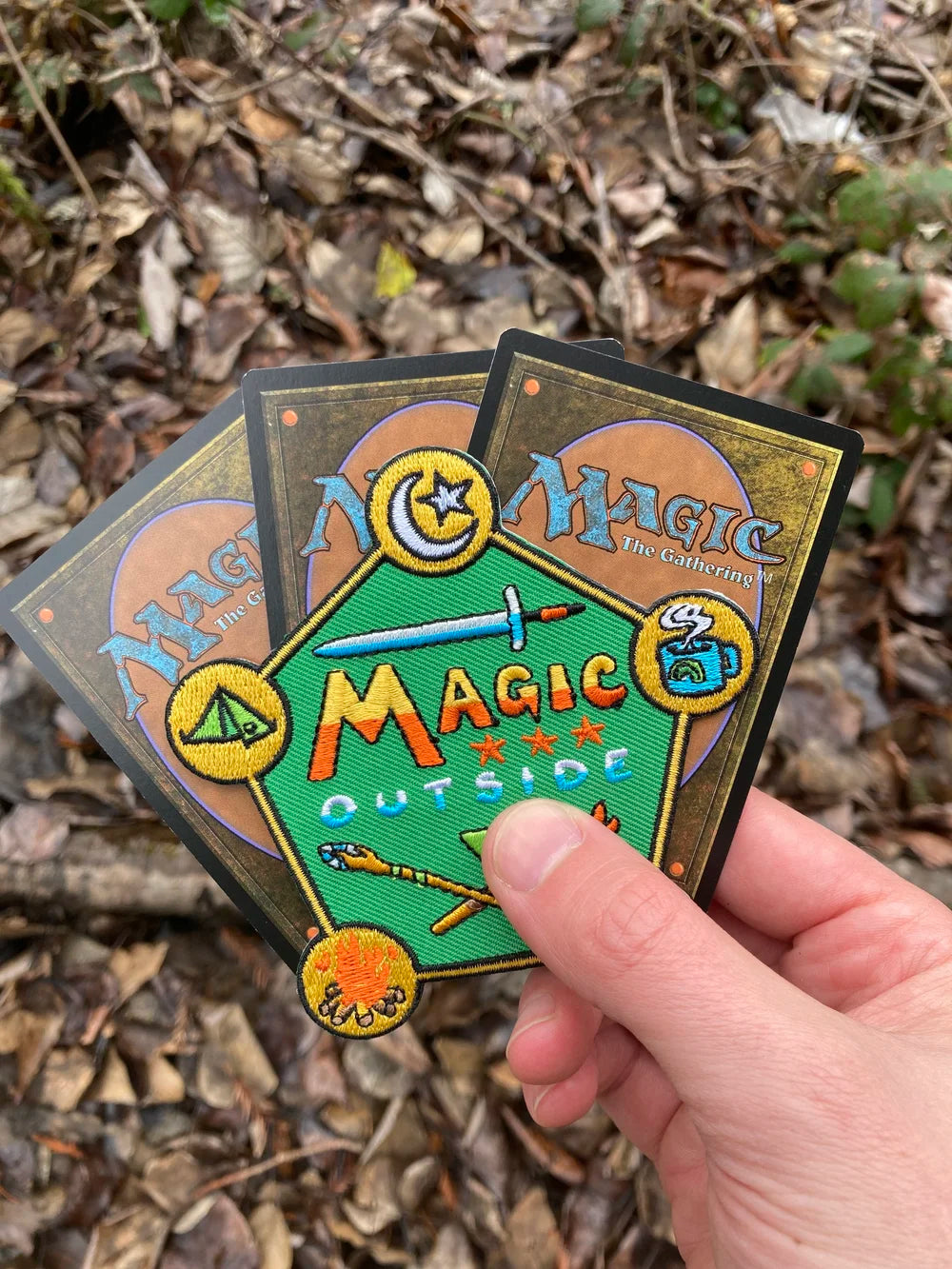 Three 'Magic: The Gathering' cards held by a hand on a natural background