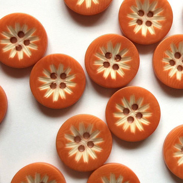 Pattern of orange buttons with floral center design on a white background