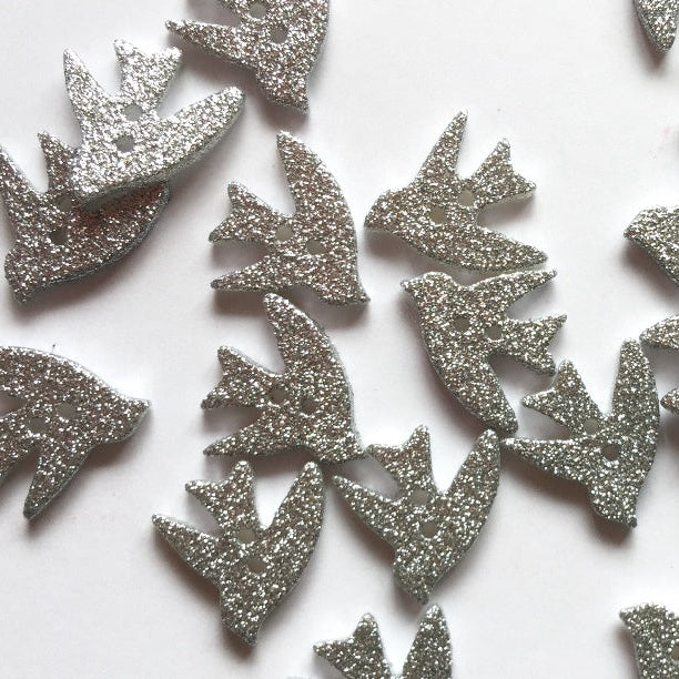Silver glittery bird buttons on a white background